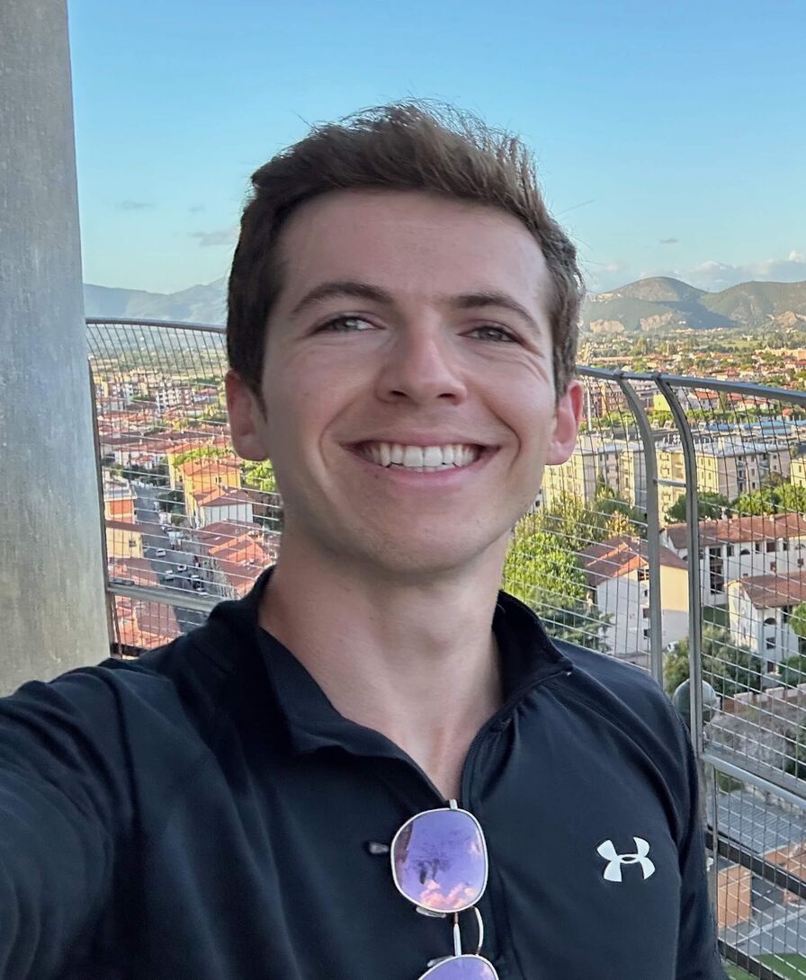 Ben's own selfie: smiling selfie on a balcony above a city in a black quarter-zip