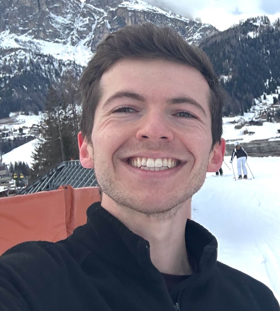 Ben's own selfie: smiling selfie on a snowy mountainside in a black zip-up