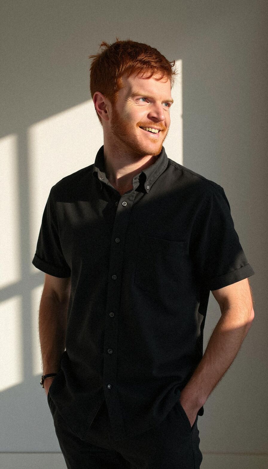 AI headshot of Cam: sunlit wall, black short-sleeve shirt (second run)