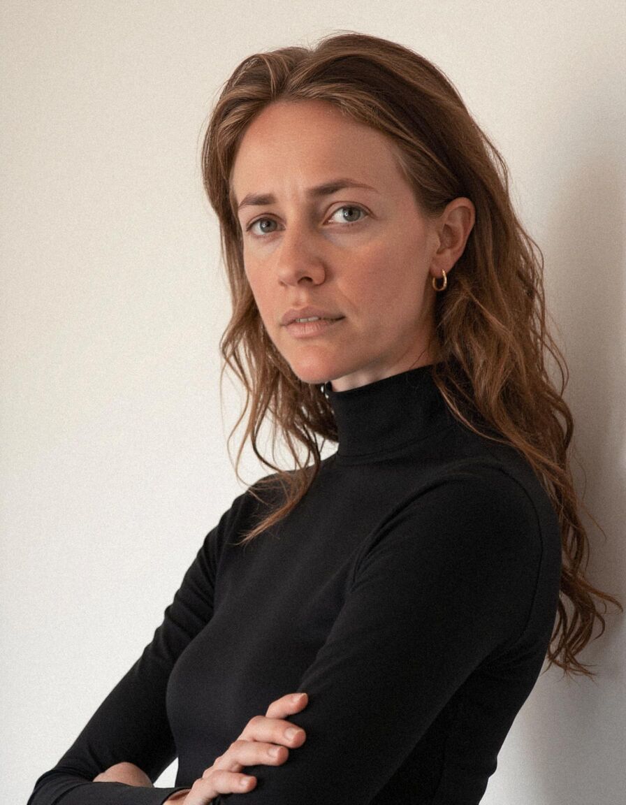 AI headshot of Hannah: plain wall, black roll-neck, arms crossed
