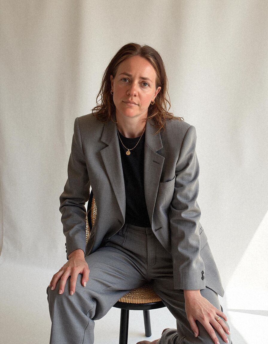 AI headshot of Hannah: studio, on a chair, grey suit