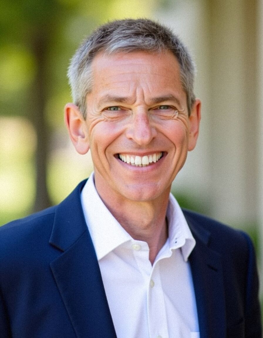 AI headshot of Rob: outdoors by trees, navy blazer and open-neck white shirt